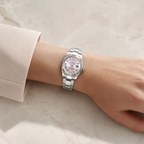 A silver-tone stainless steel watch with a pink dial and a matching pink mother-of-pearl bracelet, shown worn on a person's wrist against a light beige marble background.