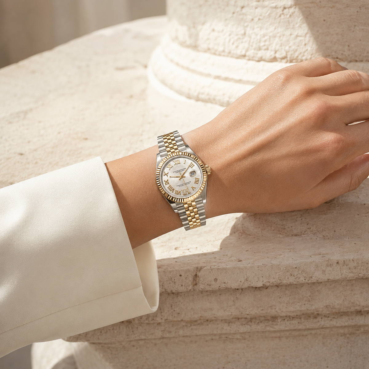 A two-tone silver and gold wristwatch with a white dial is worn on a woman's wrist, resting against a light beige stone column.