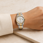 A two-tone stainless steel and gold wristwatch with a white dial and Roman numeral hour markers, shown worn on a person's wrist.