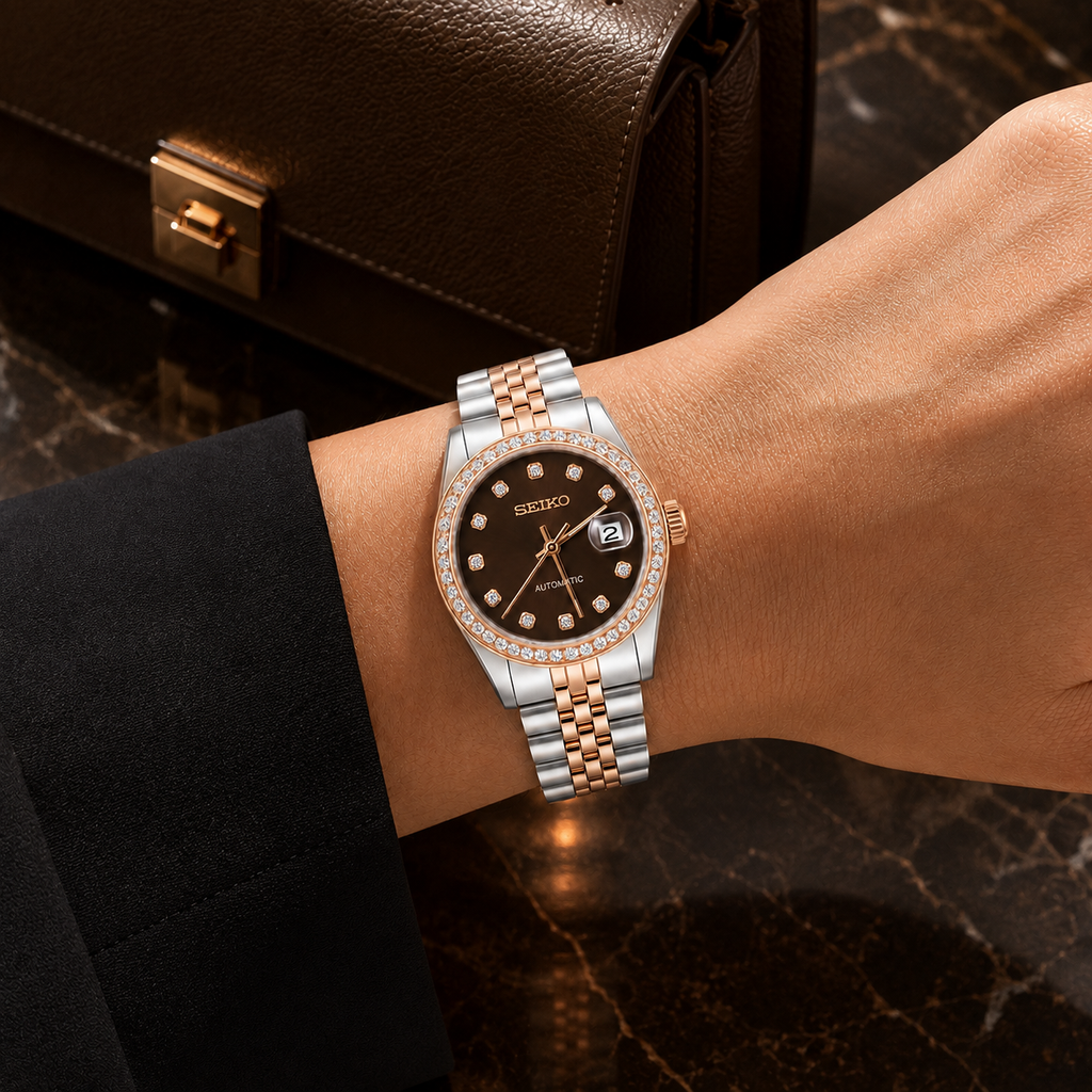 A wrist wearing a Seiko stainless steel and rose gold watch with a diamond bezel and black dial, shown against a dark marble surface with a brown leather bag in the background.