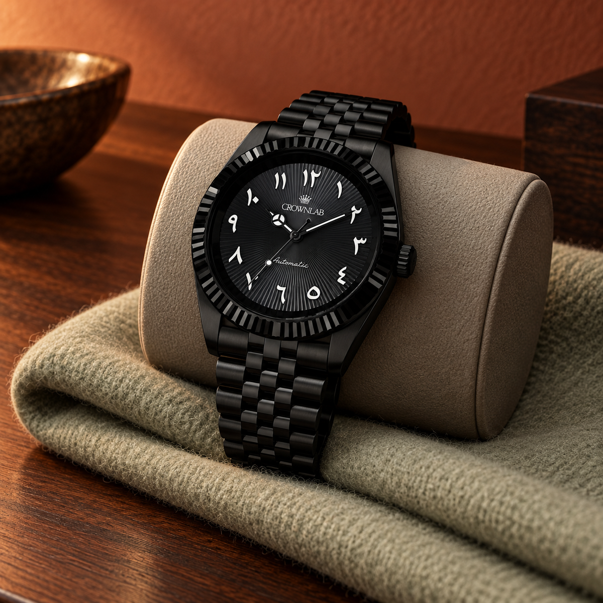 Black PVD Arabic numeral watch on a midnight-blue travel cushion over pale travertine