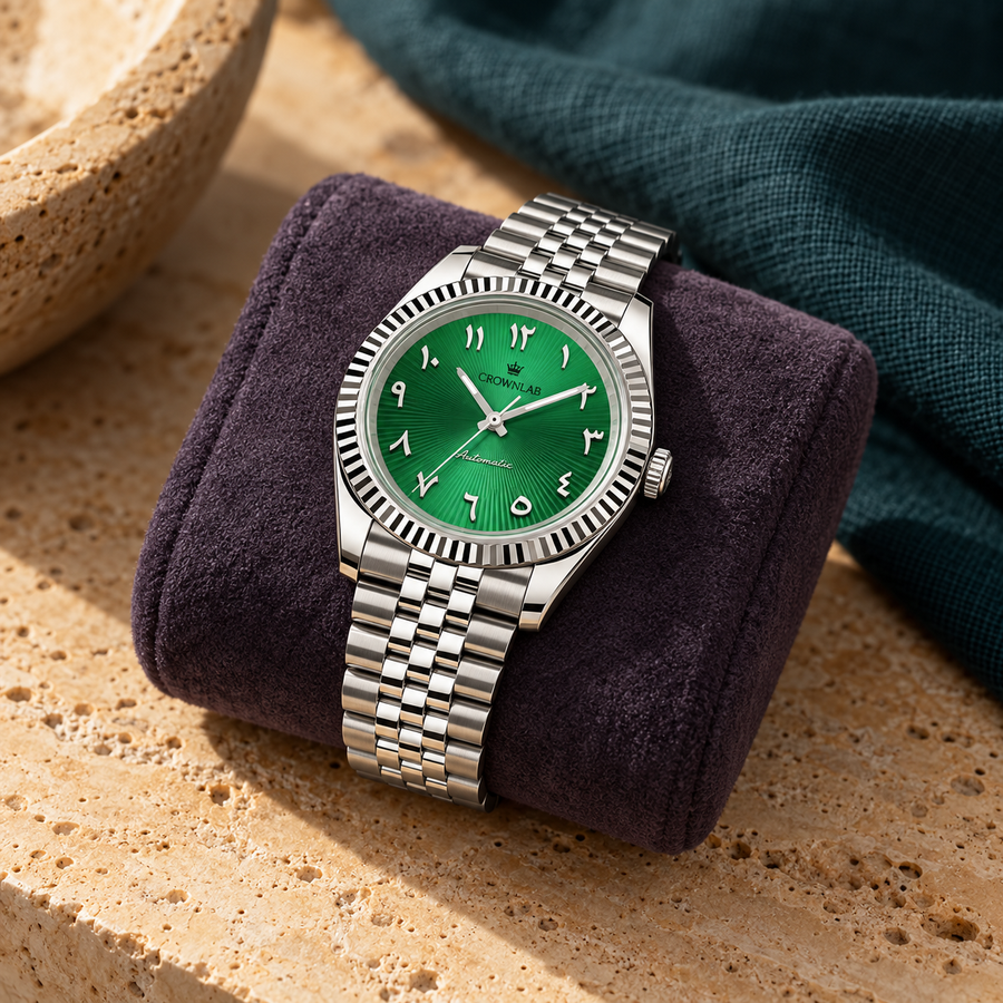 Emerald green Arabic numeral watch on dark plum suede over warm travertine, teal studio backdrop