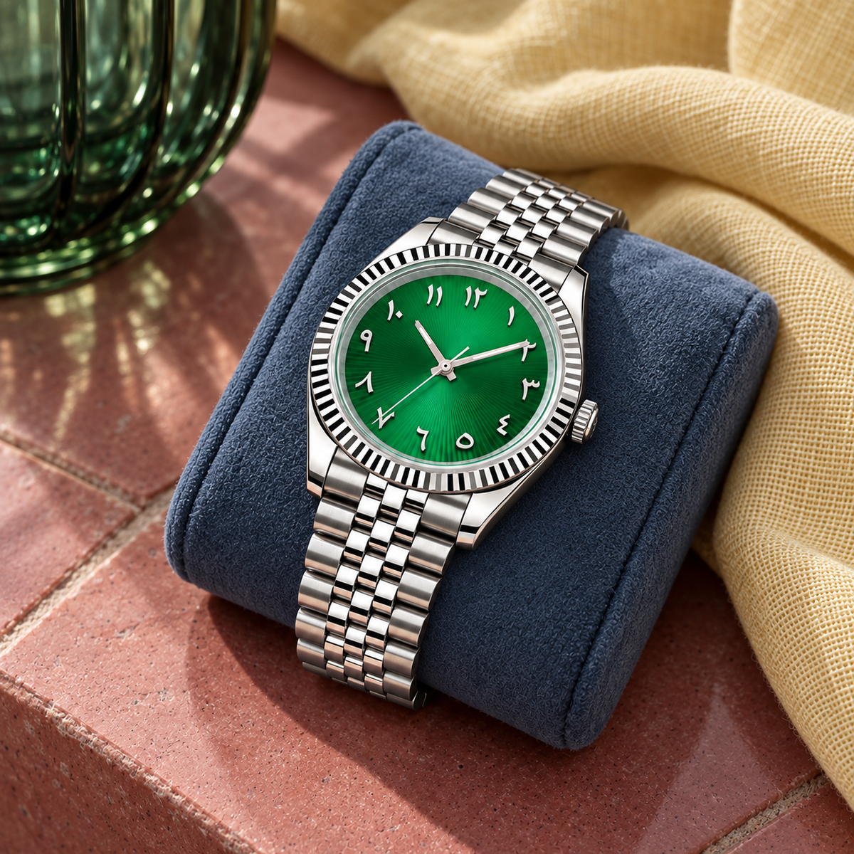Emerald green dial watch on slate-blue cushion with rose-clay stone, green glass and yellow linen