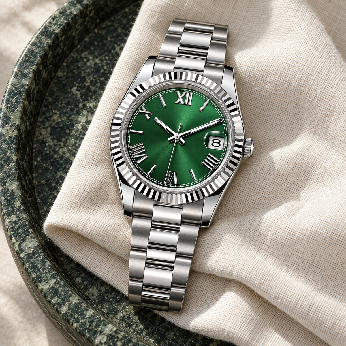 Forest-green date watch with three-link steel bracelet on cream linen and moss stone