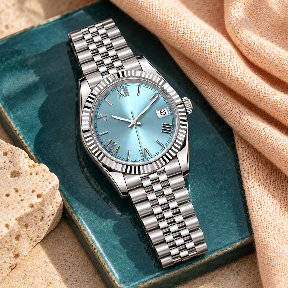 Crown Numeral Date Ice Blue laid on teal ceramic and peach linen with Jubilee bracelet