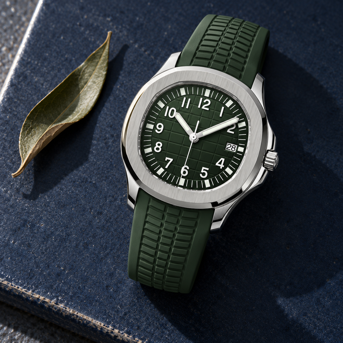 Nautiko Forest Green watch laid on midnight-blue ceramic beside an olive leaf