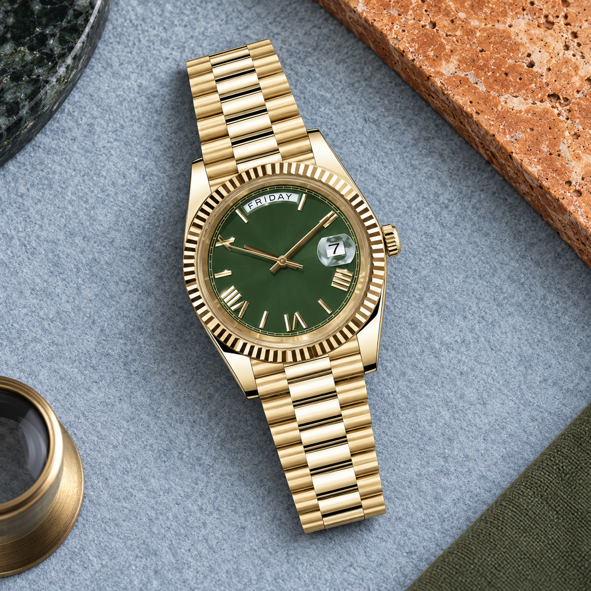 Gold Roman Olive watch flatlay on blue-gray felt and warm travertine