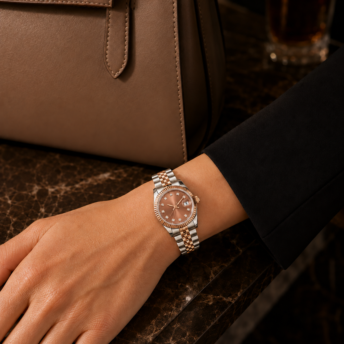 Lady Crownline Rose Blush Two-Tone watch worn with a black sleeve beside a brown leather handbag and dark marble.